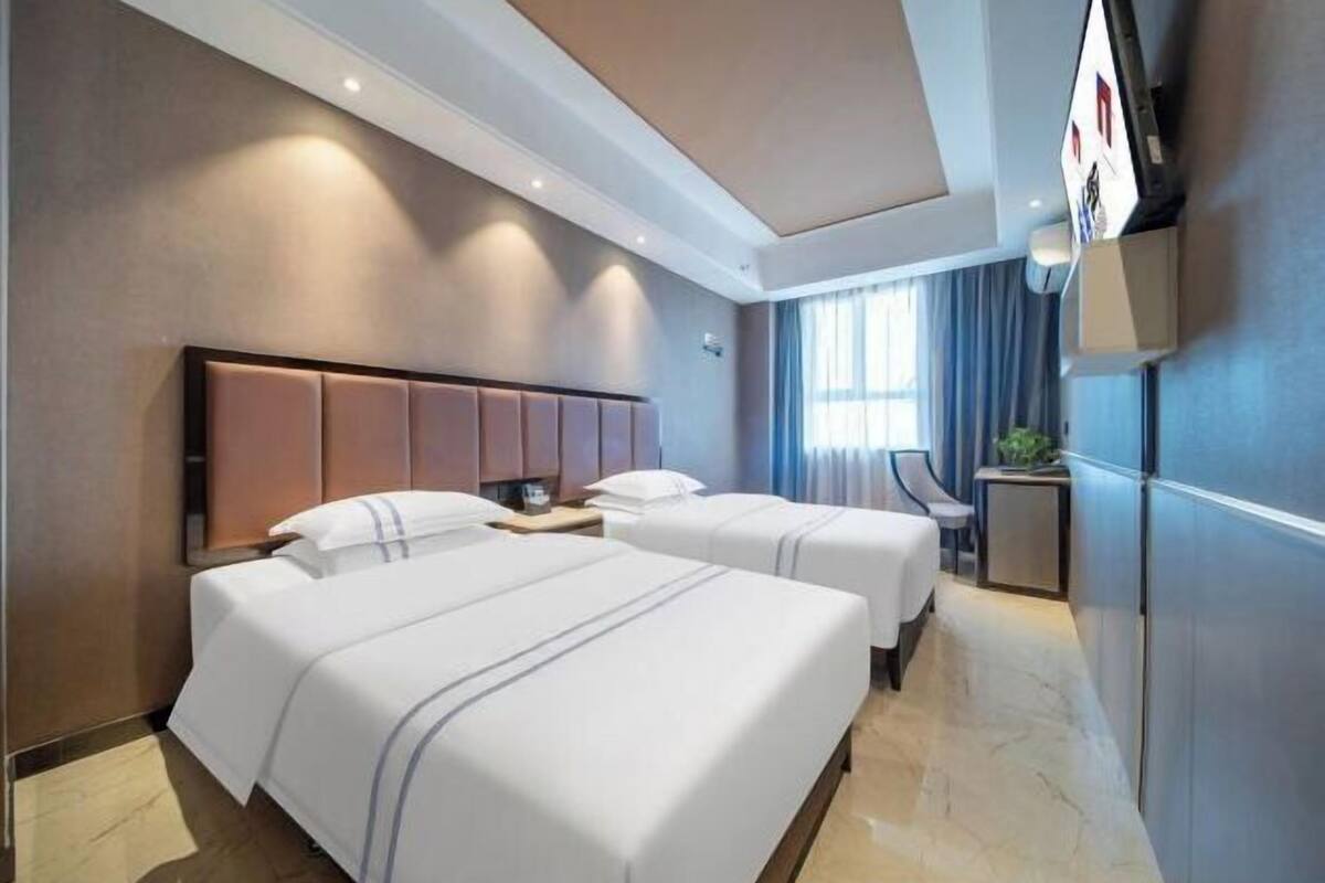 Ein Hotelzimmer mit zwei Betten, einem Flachbildfernseher, einem Schreibtisch und einem Fenster mit Vorhängen.