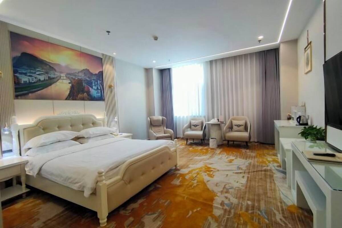 Habitación de hotel con cama, escritorio, silla, televisor y un cuadro en la pared.