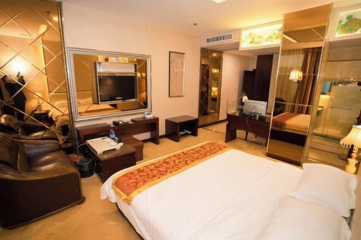 Habitación de hotel con una cama grande, televisión, escritorio y zona de estar con sofá de cuero.