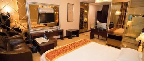 A hotel room with a large bed, a television, a desk, and a seating area with a leather couch.