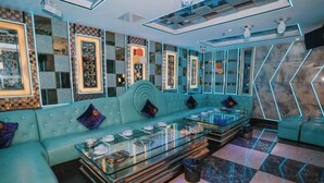 Un espacio lounge moderno con un sofá azul verdoso, una mesa de centro de vidrio y decoración en la pared.