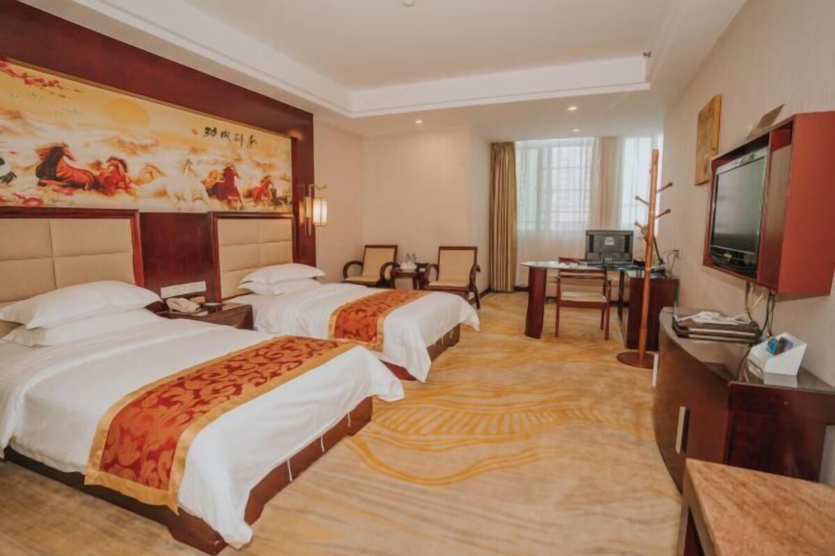 A hotel room with two beds, a desk, a television, and a painting on the wall.
