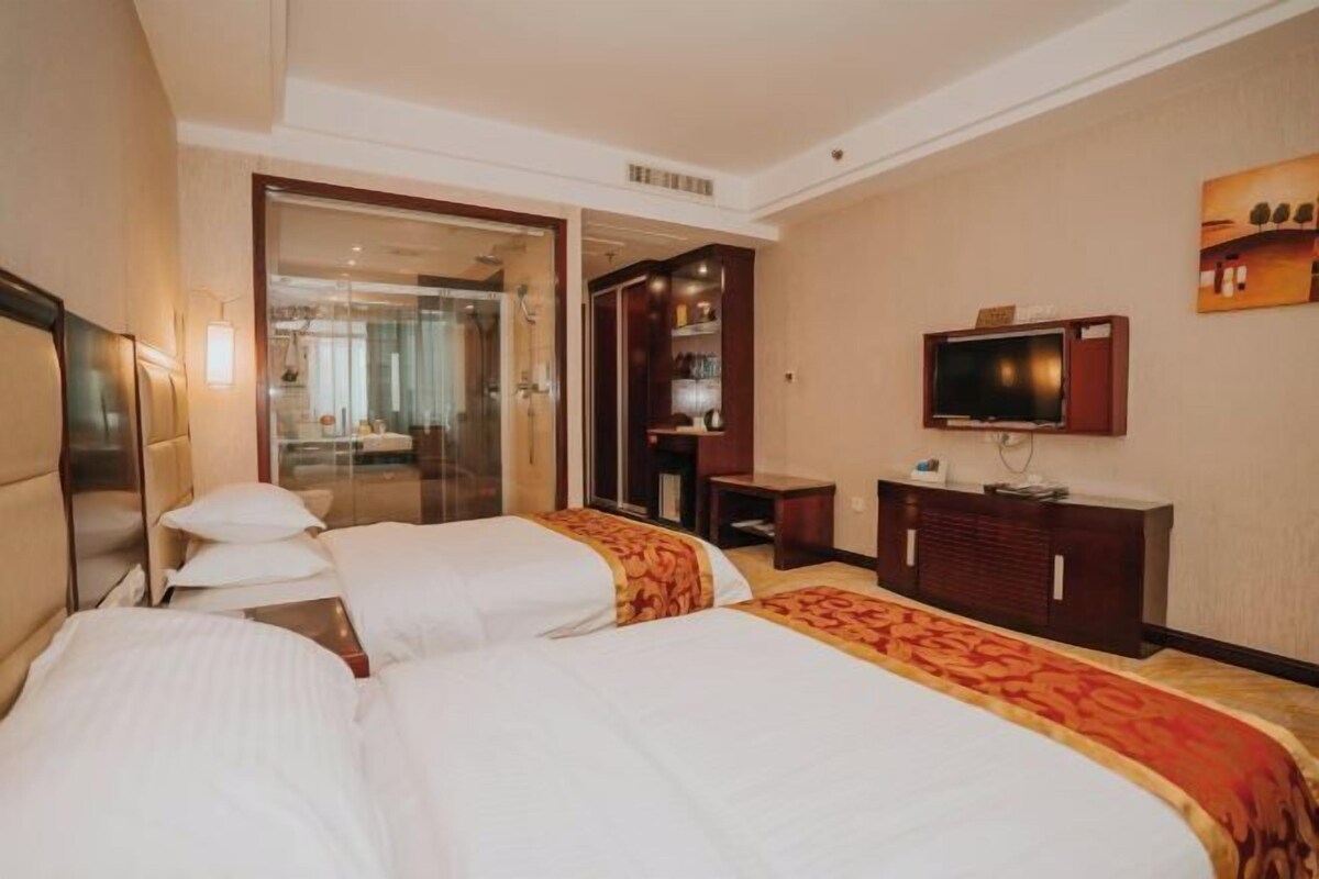 A hotel room with two beds, a television, a wardrobe, and a bathroom visible through an open door.