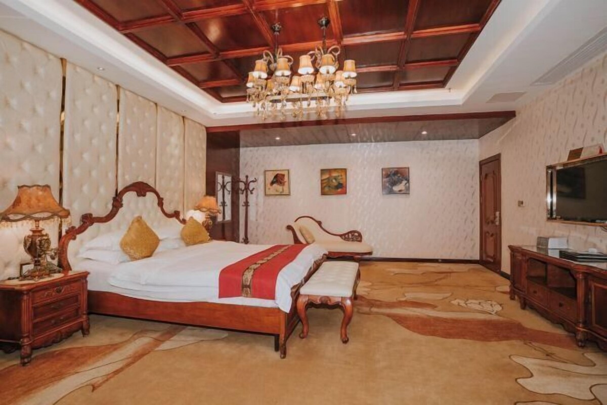 A spacious bedroom with a large bed, a wooden bench, a TV, and a chandelier.