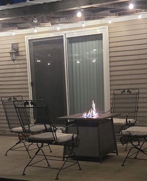 Une terrasse extérieure avec des chaises en métal, une table et un foyer.