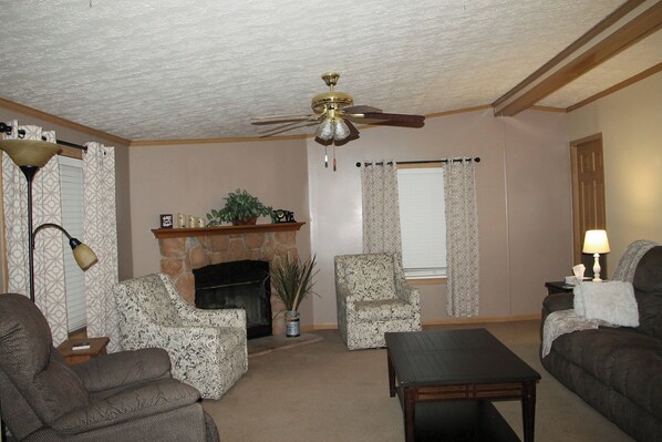 A living room with a fireplace, two patterned armchairs, a sofa, a coffee table, and a ceiling fan.