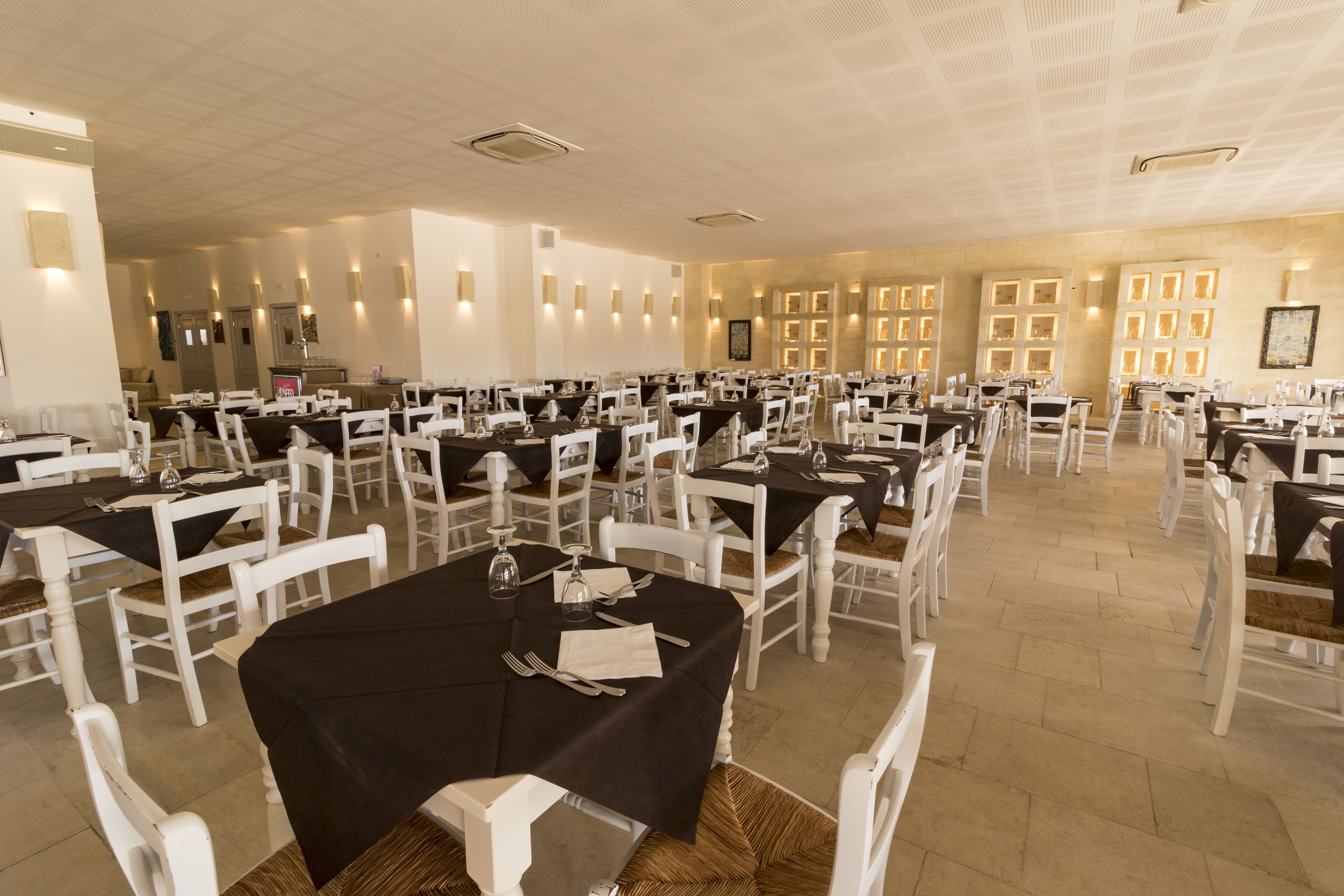 A spacious banquet hall with multiple round tables, each set with white chairs and black tablecloths.