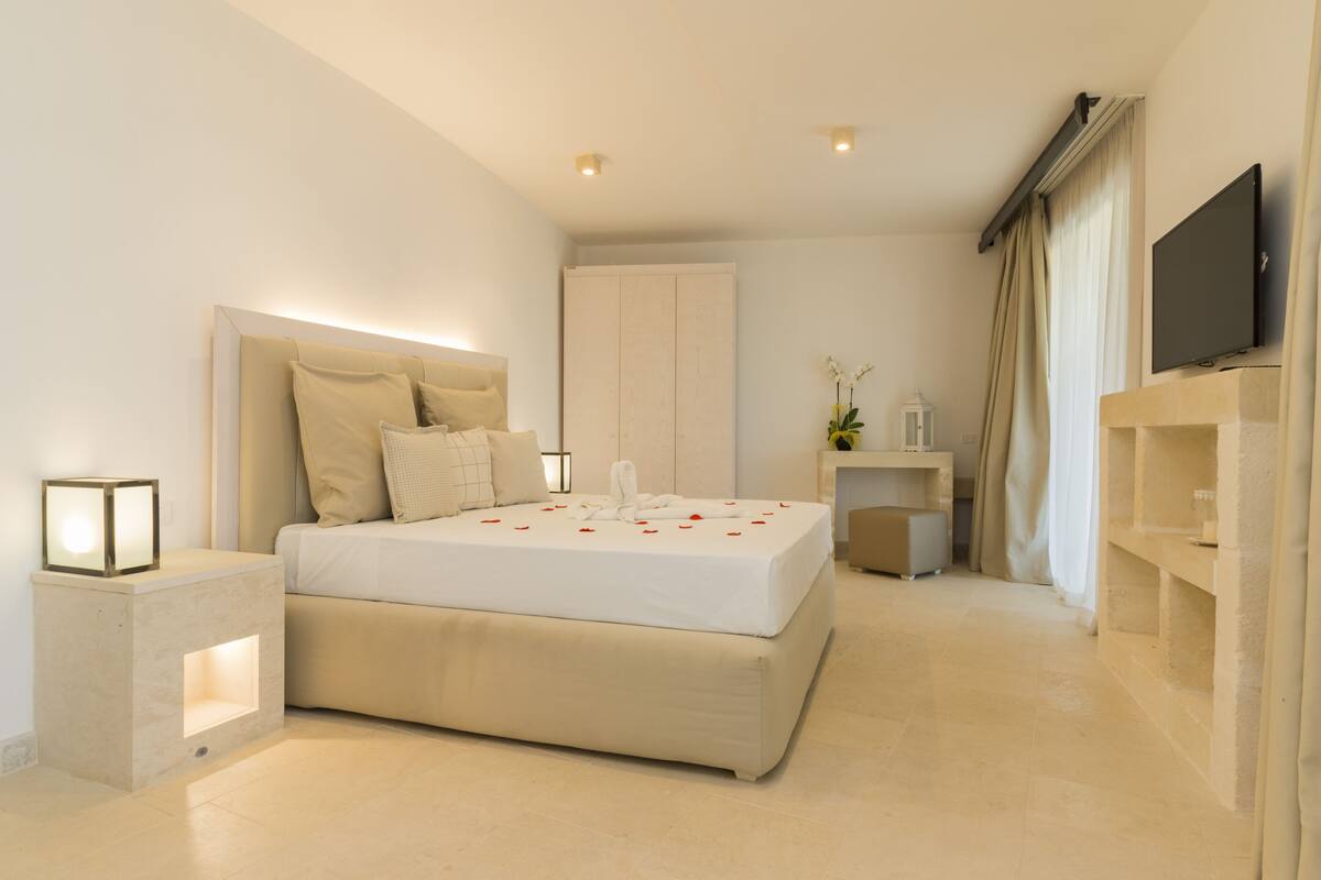 Une chambre d’hôtel moderne dotée d’un grand lit, de tables de chevet, d’un téléviseur à écran plat et d’une petite table d’appoint avec une lampe.