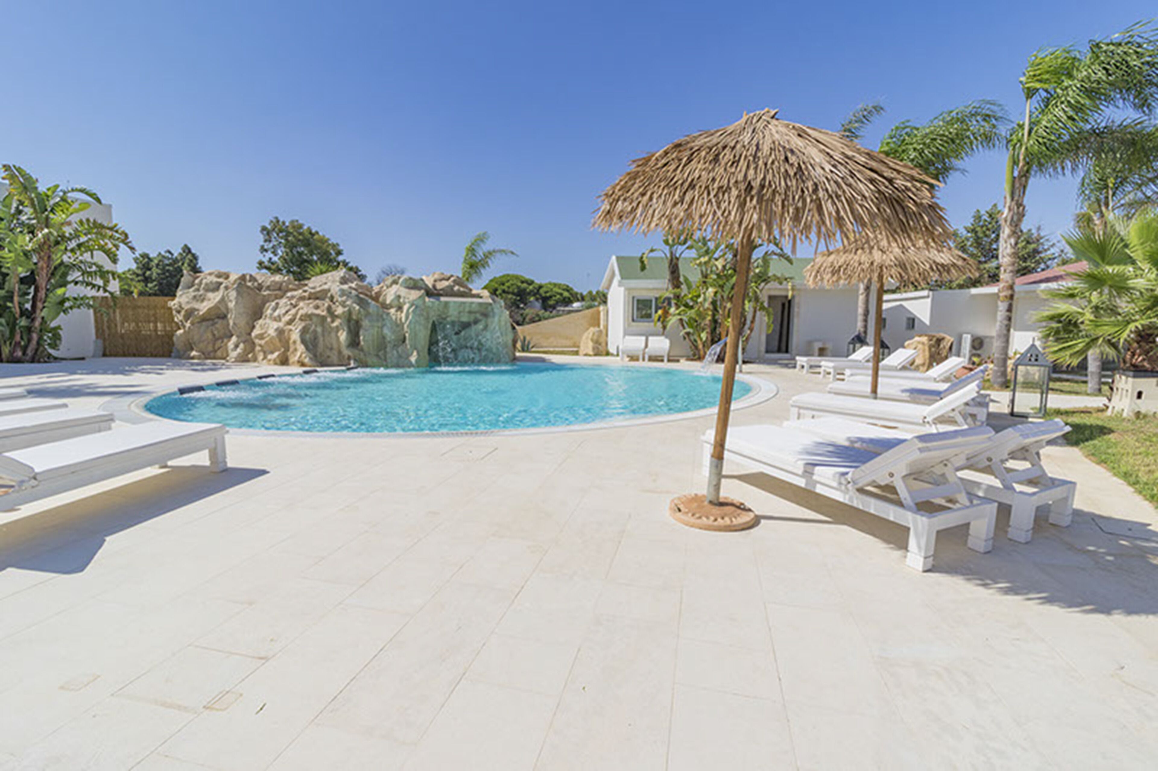 A pool area with lounge chairs, a thatched umbrella, and a rocky water feature.