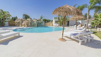 A pool area with lounge chairs, a thatched umbrella, and a rocky water feature.