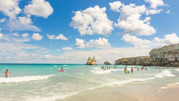Ein Strand mit klarem türkisblauem Wasser, Felsformationen und Menschen, die schwimmen und entspannen.