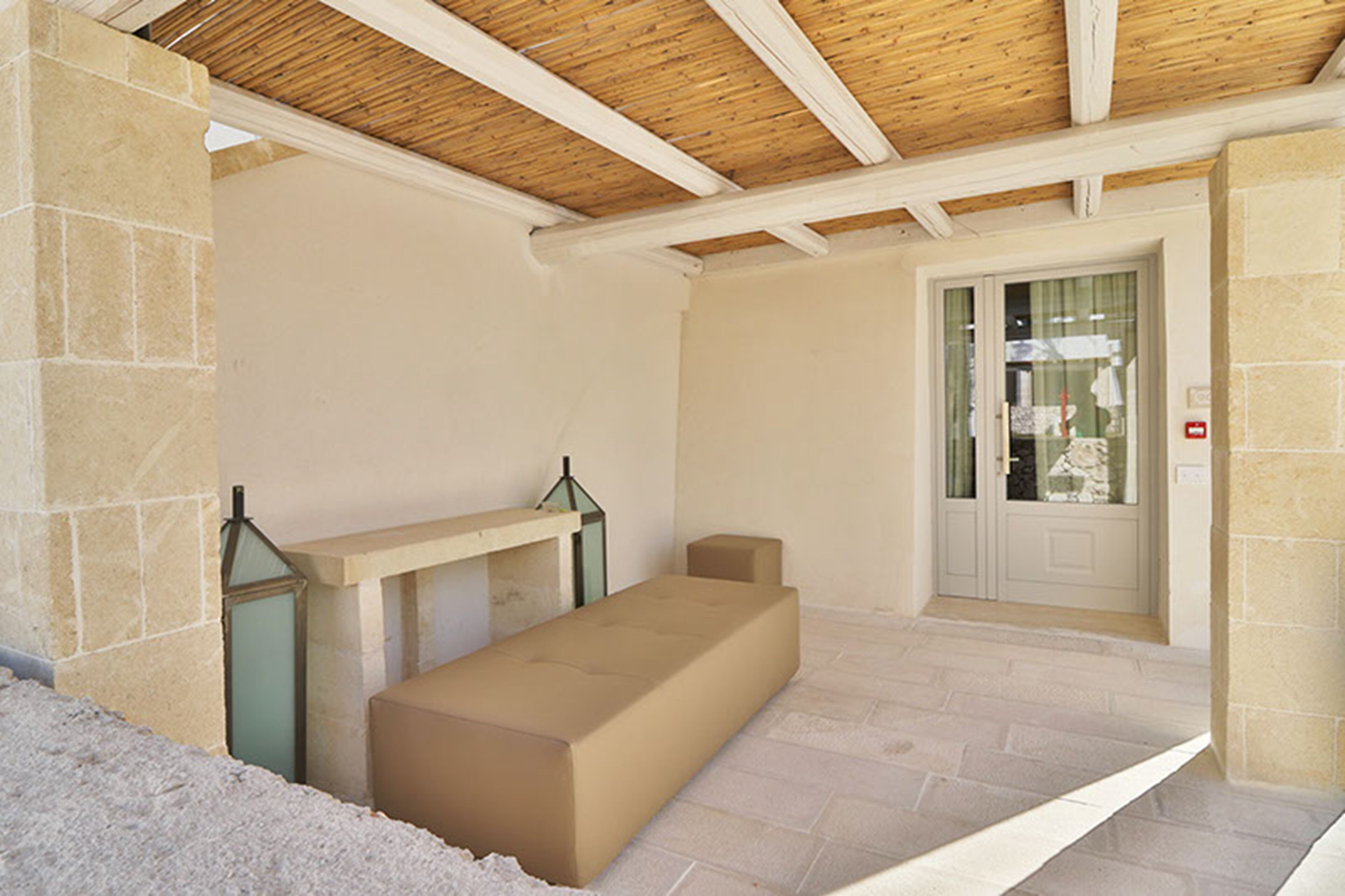 A room with a stone wall, a bench, a door with glass panels, and a wooden ceiling.