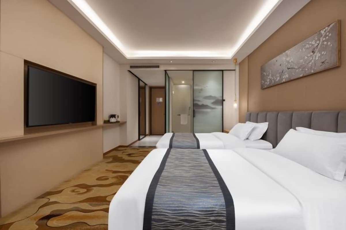 A hotel room with a large bed, a flat-screen TV mounted on the wall, a painting, and a carpeted floor.