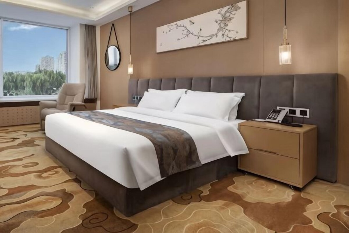 A hotel room with a large bed, bedside table, and a view of the city.