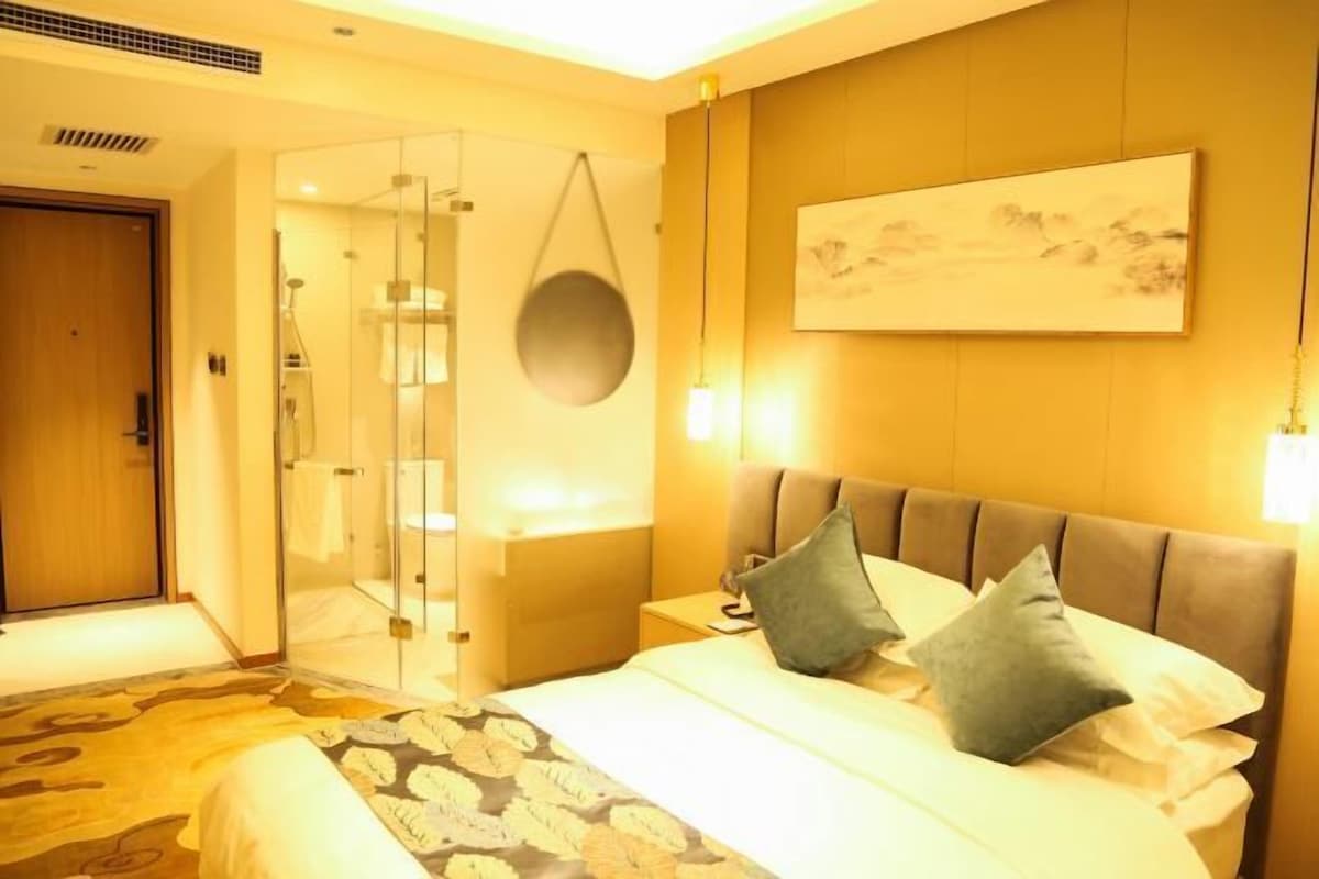 A hotel room with a bed, bedside table, and a glass shower enclosure.