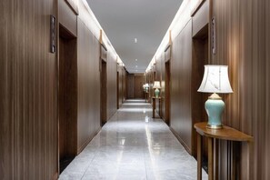 A hotel corridor with wooden paneling, marble flooring, and wall-mounted lamps. - Botai Hotel (Yongqing)