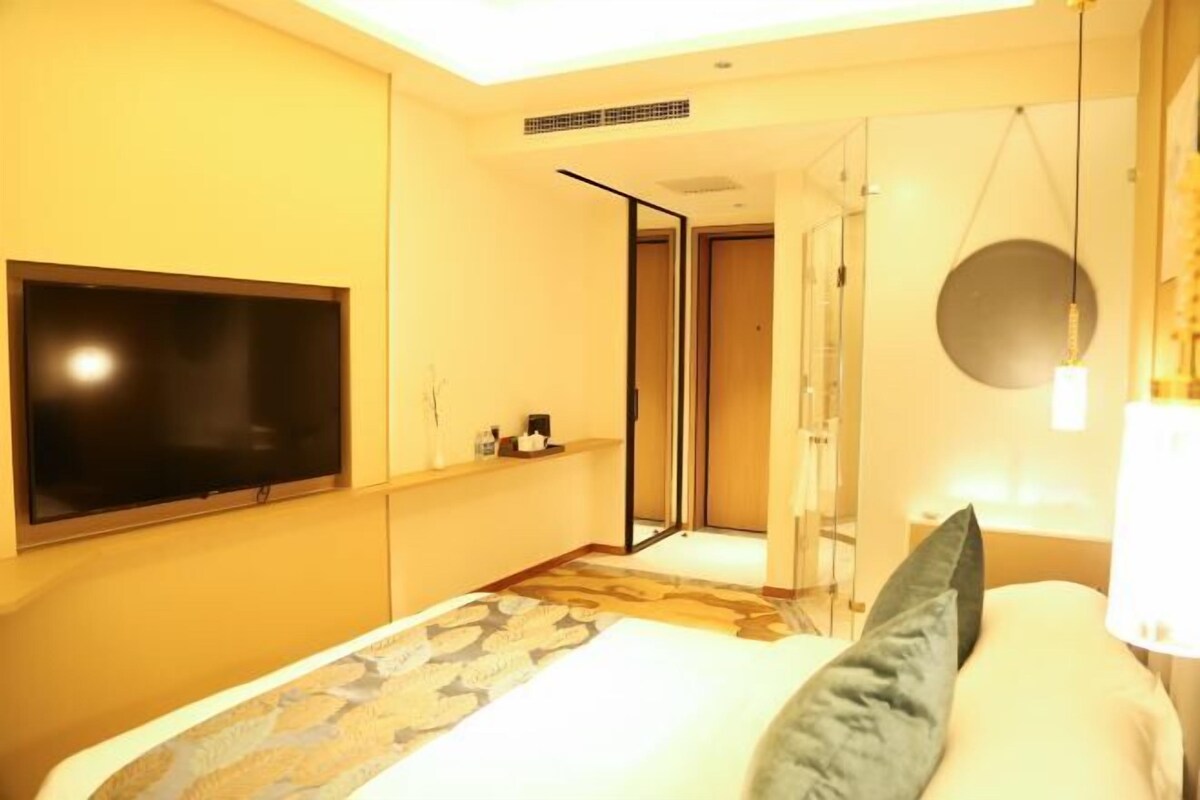 A hotel room with a large bed, a flat-screen TV mounted on the wall, a mirror, and a door leading to another room.