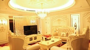 Una sala de estar lujosa con un televisor grande, muebles blancos ornamentados y un candelabro.