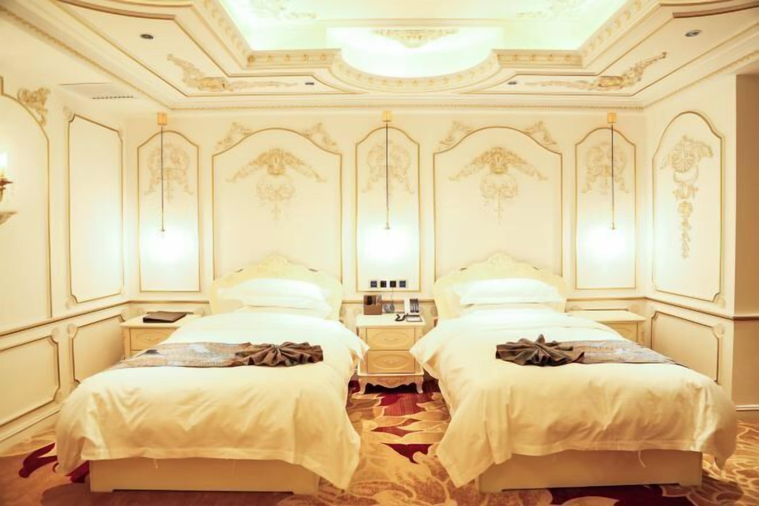 A hotel room with two beds, a chandelier, and ornate wall decorations.