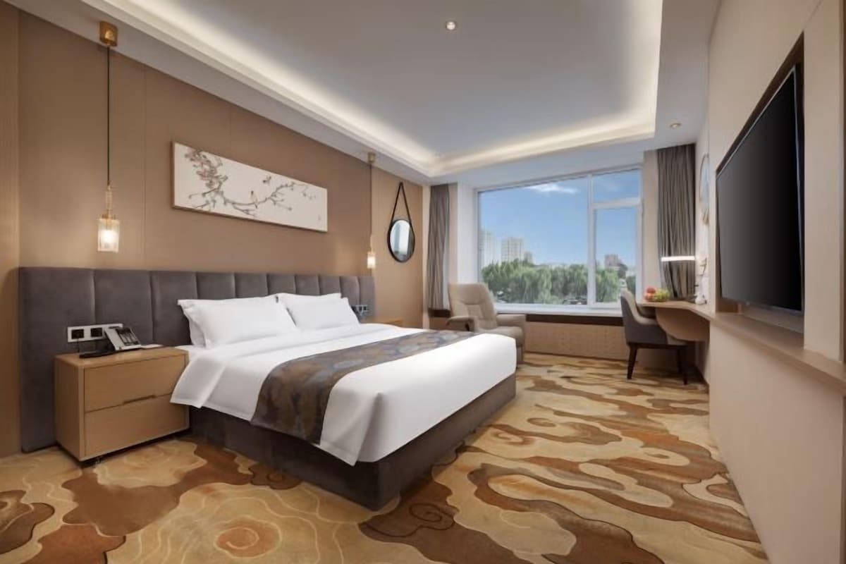 A hotel room with a large bed, a desk, and a view of the city.