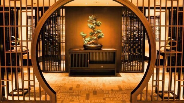 Una habitación tradicional japonesa con suelo de tatami, un mueble de madera bajo y un bonsái.