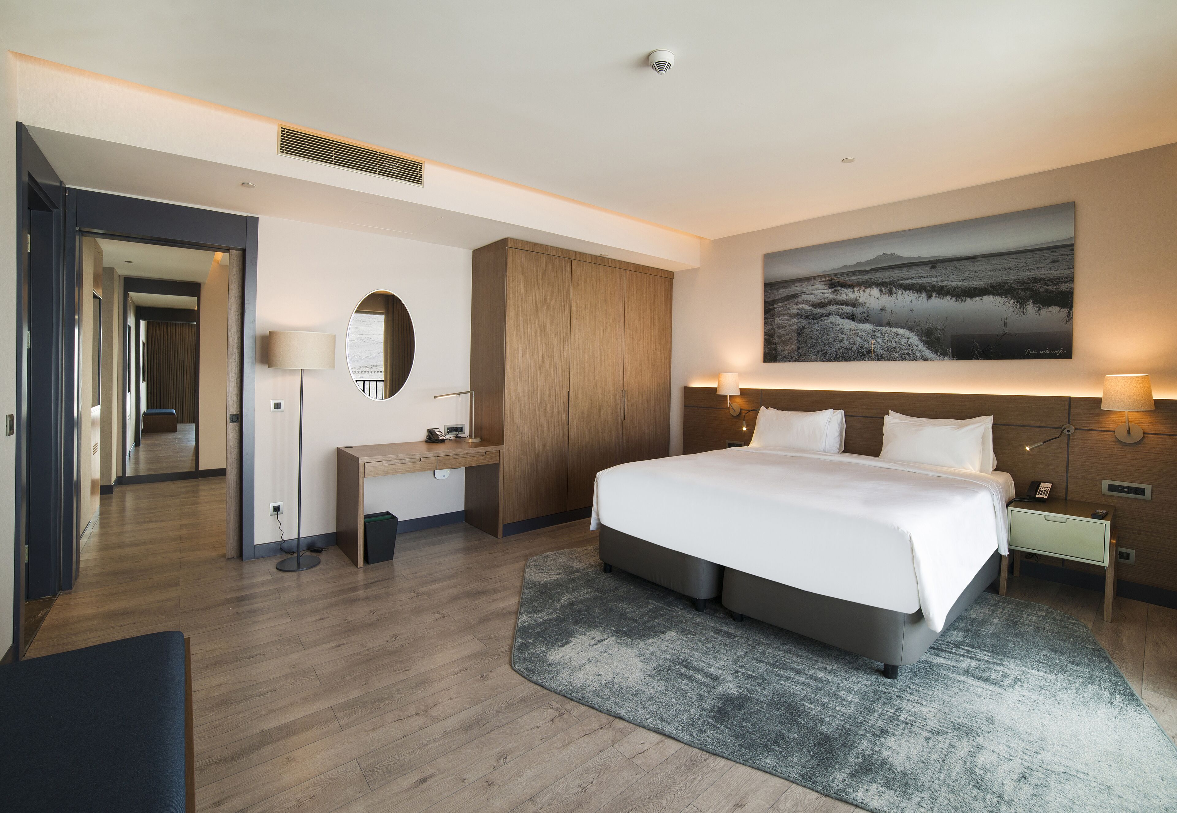 Moderni hotellihuone, jossa on suuri sänky, työpöytä, vaatekaappi ja taulu seinällä.