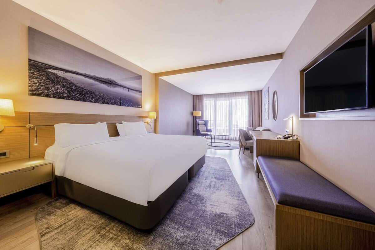 Habitació d'hotel moderna amb un llit gran, un escriptori, una banca i una televisió.