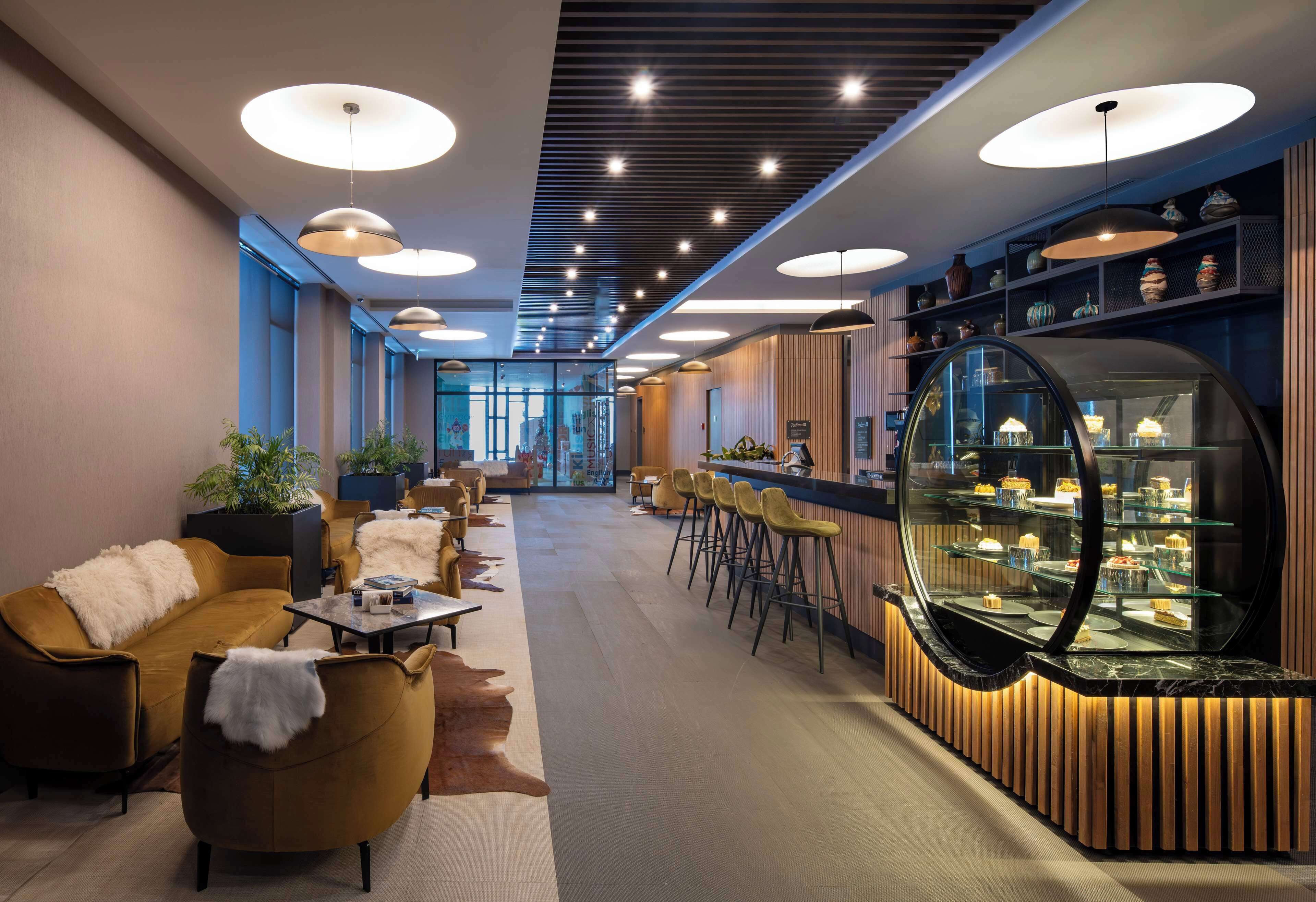 Un moderno vestíbulo de hotel con áreas de descanso, un bar con vitrina de cristal e iluminación empotrada en el techo.