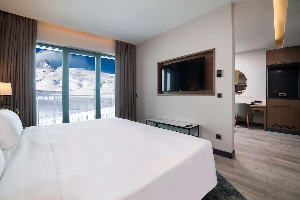 Habitació d'hotel amb un llit gran, una taula de treball, una televisió i vista a una muntanya nevada.