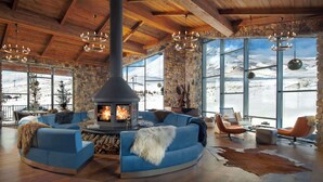 A cozy living room with a stone fireplace, blue sofas, and a large window offering a snowy mountain view. - Radisson Blu Hotel, Mount Erciyes (Kayseri)
