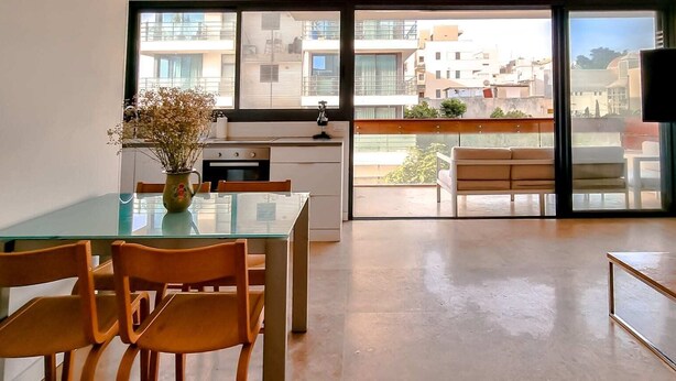 A modern kitchen with a glass dining table and chairs, a vase with flowers, and a view of the city through large windows. - Apt Ophrys 1BR Tel Aviv Kalisher St TL66 (Tel Aviv)