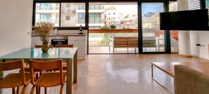 A modern kitchen with a glass dining table and chairs, a vase with flowers, and a view of the city through large windows. - Apt Ophrys 1BR Tel Aviv Kalisher St TL66 (Tel Aviv)