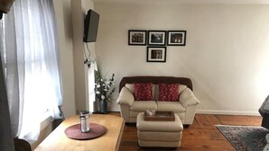 Uma sala de estar com uma mesa de madeira, um sofá e uma mesa de centro. Há quatro quadros na parede.