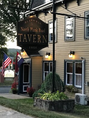 Eine historische Taverne mit einem Schild, auf dem "North Plank Road Tavern 1801" steht, und einer amerikanischen Flagge.