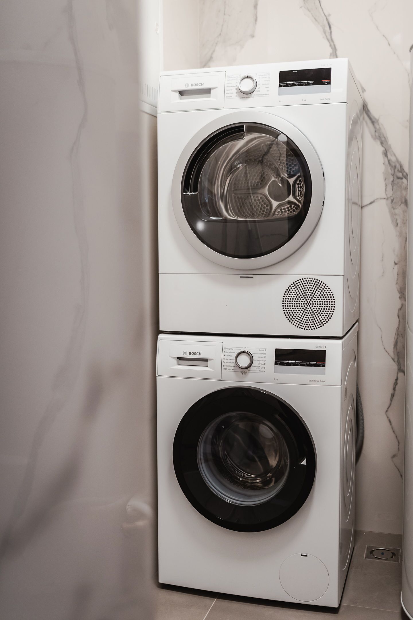 A stacked washer and dryer unit in a bathroom with a marble wall.