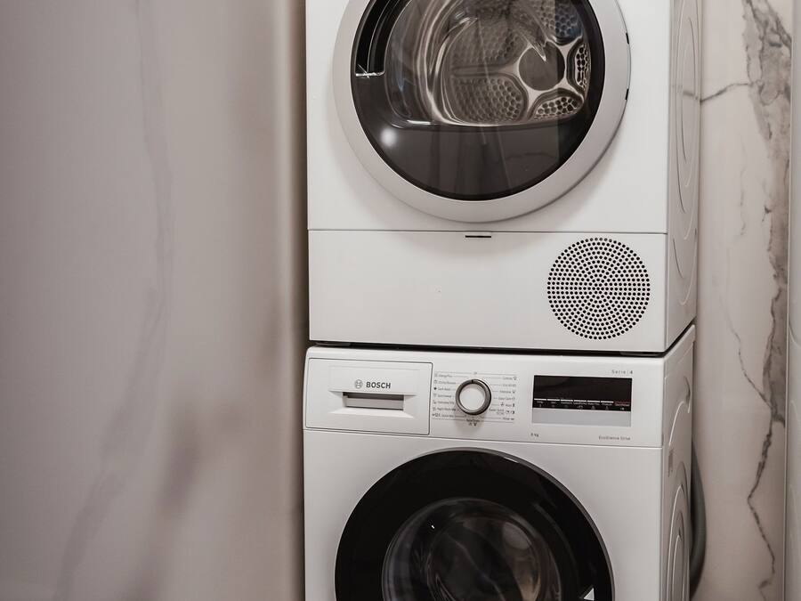 A stacked washer and dryer unit in a bathroom with a marble wall.