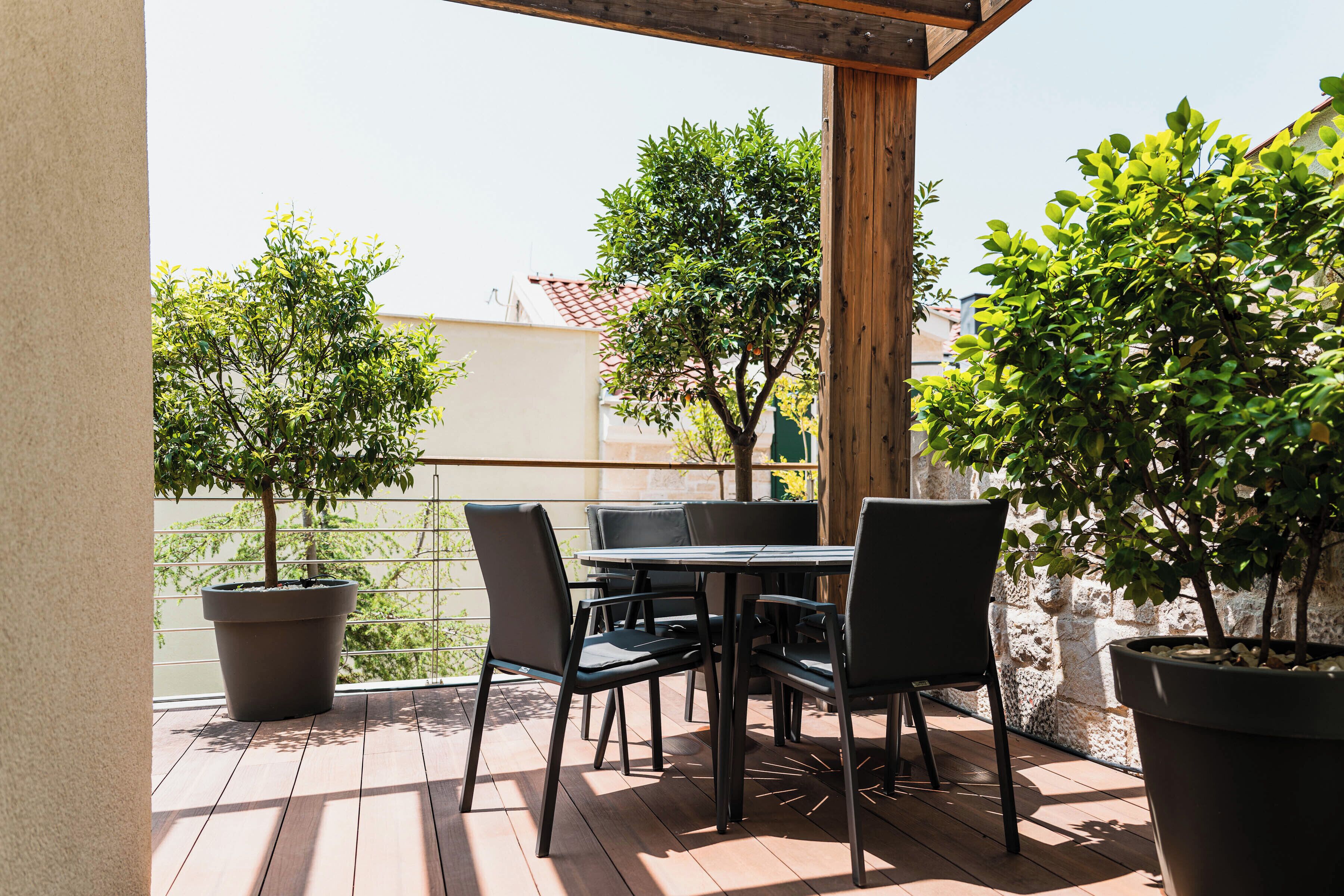 Une terrasse extérieure avec une table et des chaises, entourée de plantes en pot et d’une pergola en bois.