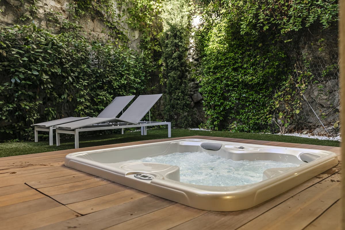 Un bain à remous sur une terrasse en bois, avec un mur en pierre et de la verdure en arrière-plan.