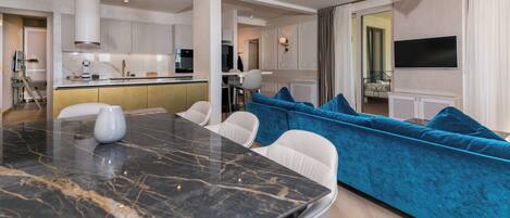 A modern living room with a marble dining table, a blue sofa, and a TV mounted on the wall.