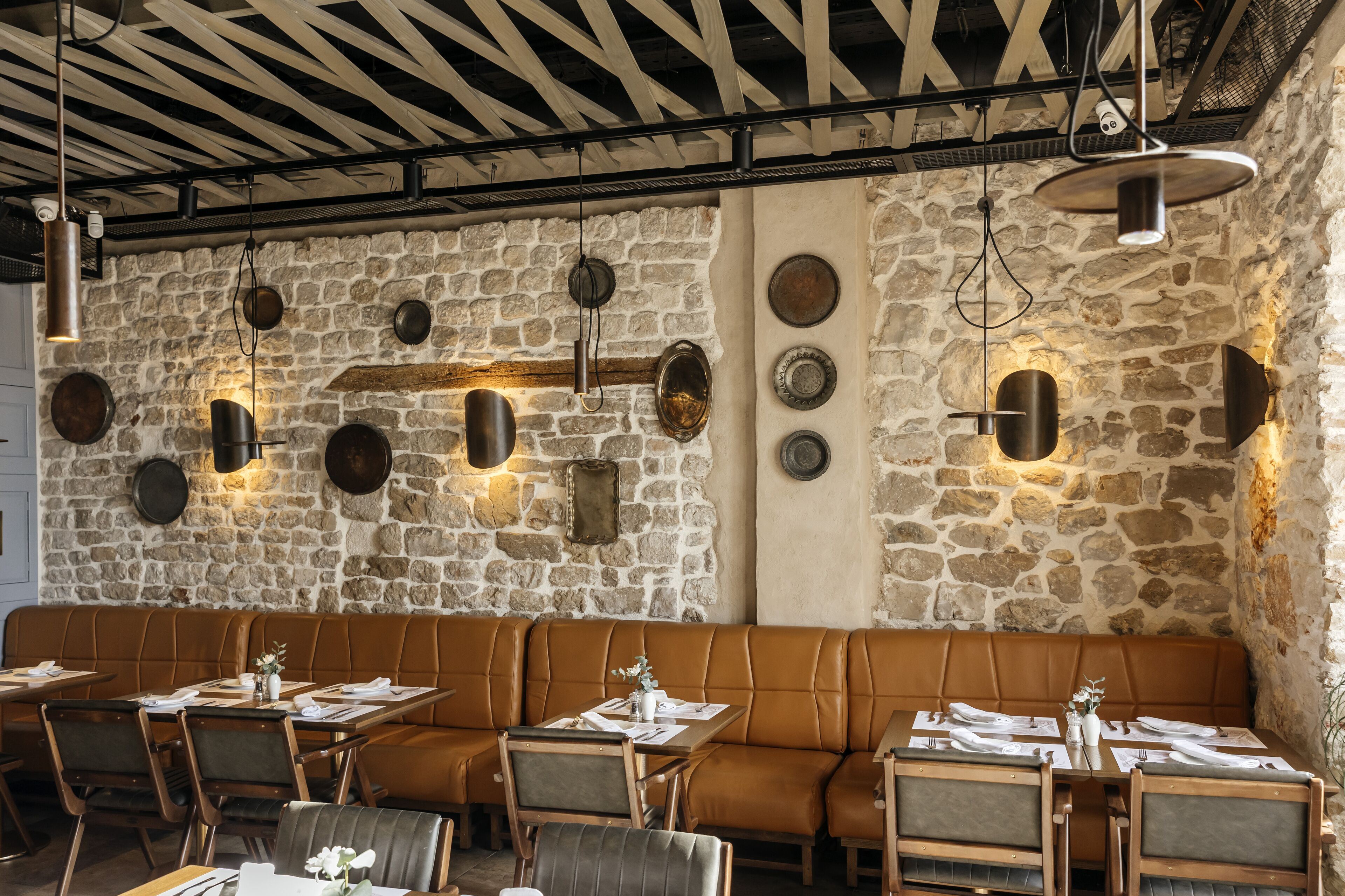 A restaurant with stone walls, leather seating, and pendant lighting.