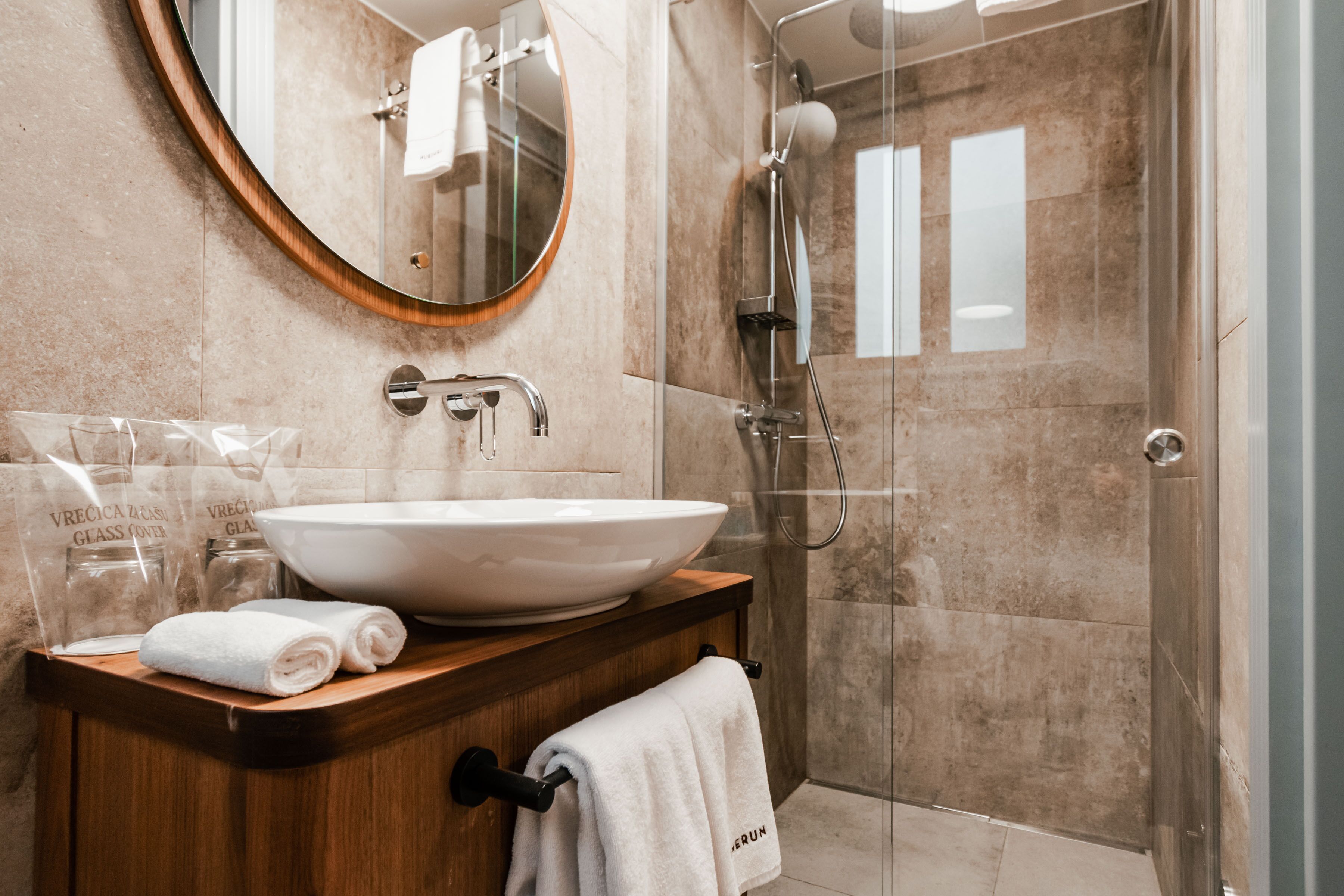 A modern bathroom with a large oval sink, a wooden vanity, a glass shower enclosure, and a mirror with a wooden frame.