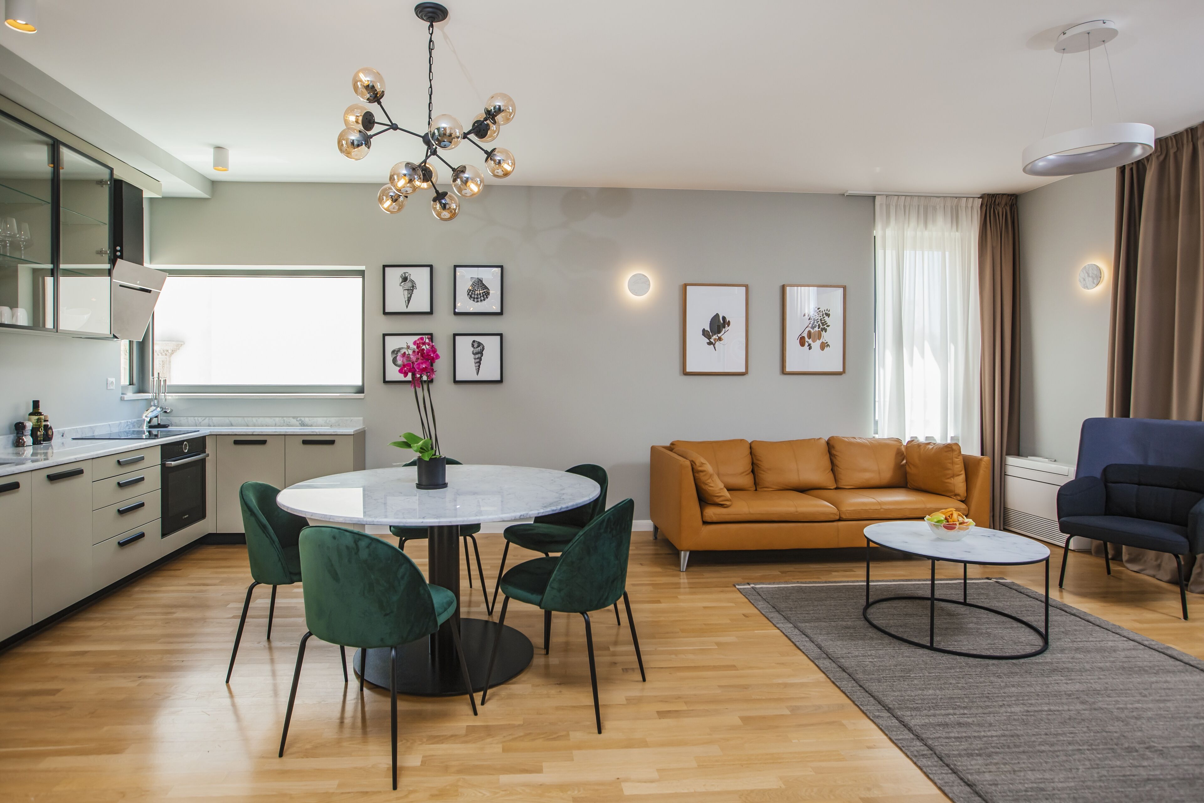 A modern living room with a round dining table, green chairs, a brown sofa, and a blue armchair.