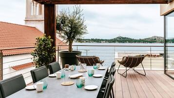 A terrace with a table set for dining, overlooking a body of water and hills.