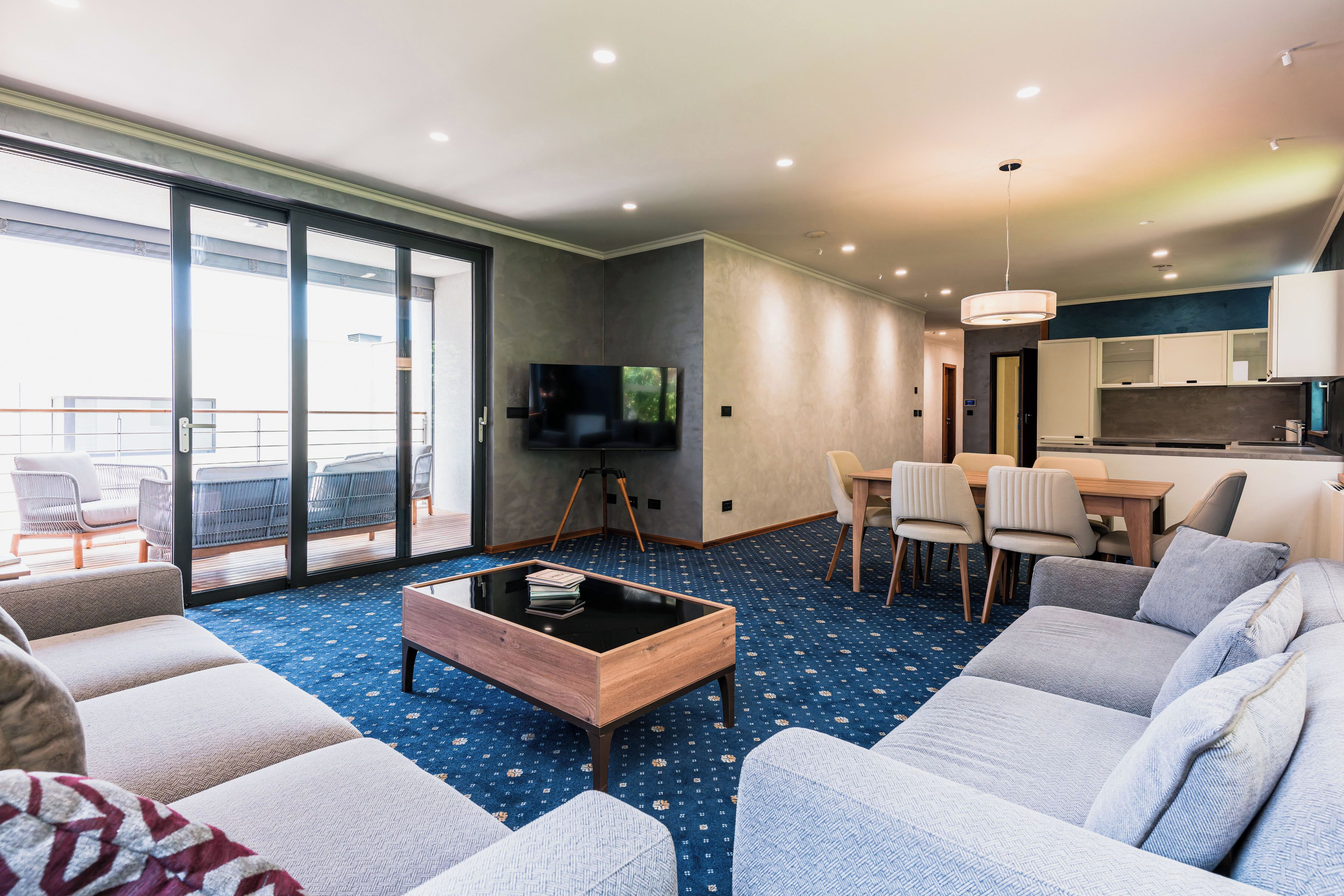 Ein modernes Hotelzimmer mit einer großen Couch, einem Couchtisch, einem Fernseher, einer Essecke mit Stühlen und einem Balkon mit Sitzgelegenheit.