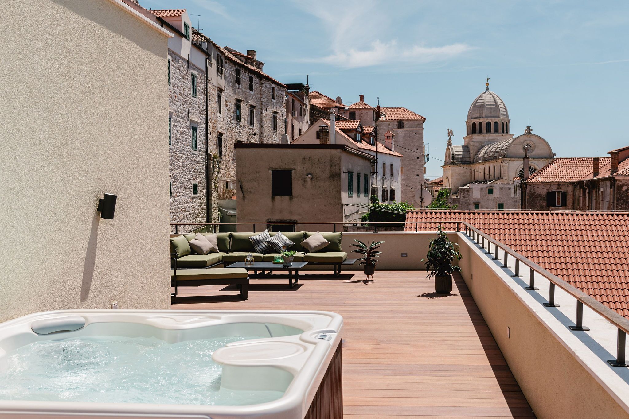 Eine Dachterrasse mit Whirlpool, Sitzgelegenheiten im Freien und Blick auf historische Gebäude.