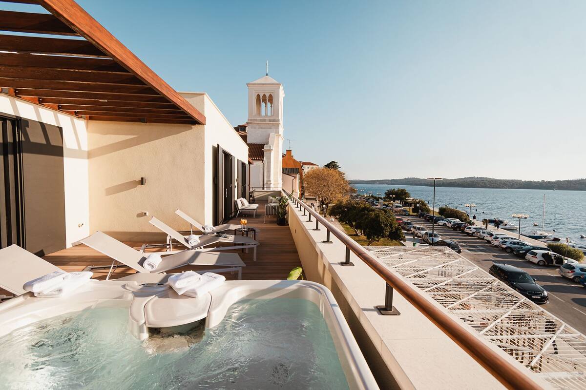 Un balcon avec un jacuzzi, des chaises longues et une vue sur la mer.