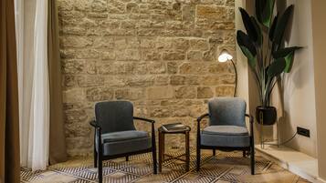 A room with two grey armchairs, a small table, a lamp, and a large plant against a stone wall.