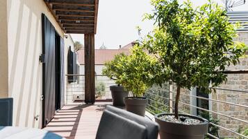 Ein Balkon mit Blumentöpfen, einer Holz-Pergola und Blick auf Gebäude im Hintergrund.
