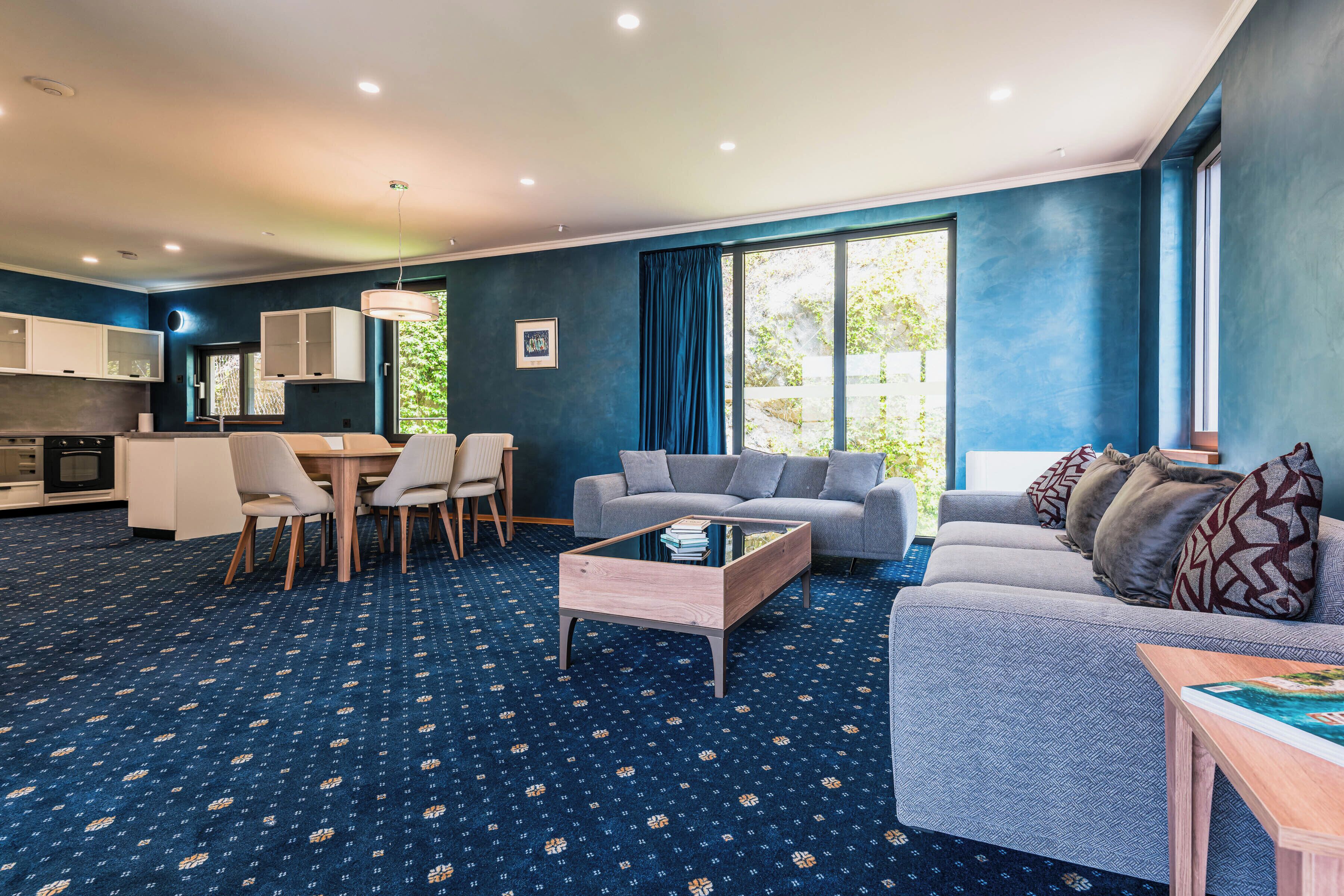 A modern living room with a blue carpet, grey sofa, and a dining area with a table and chairs.