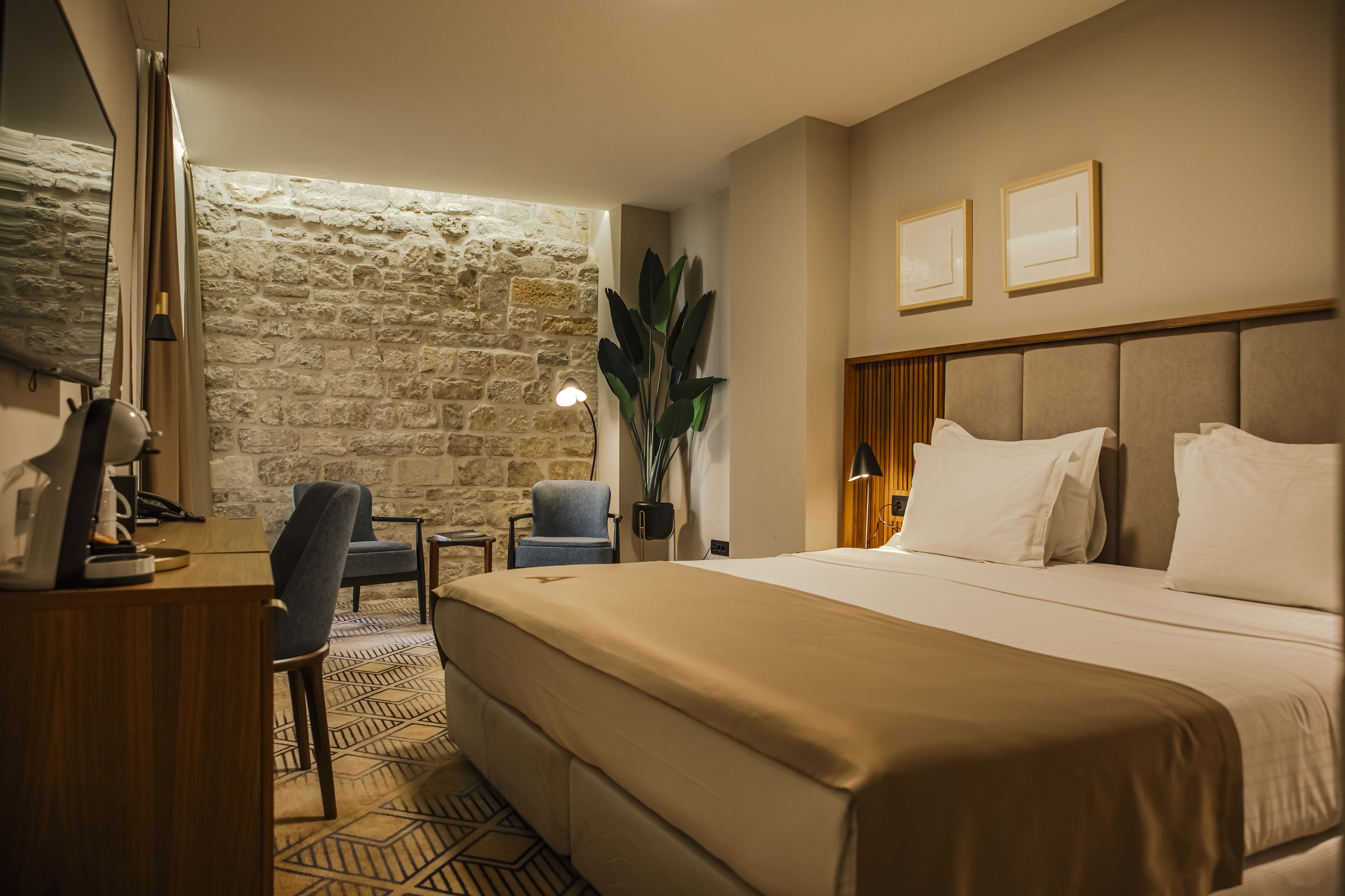 Una camera d'hotel con un letto grande, una scrivania con un computer, una sedia, un muro in pietra e due quadri appesi al muro.